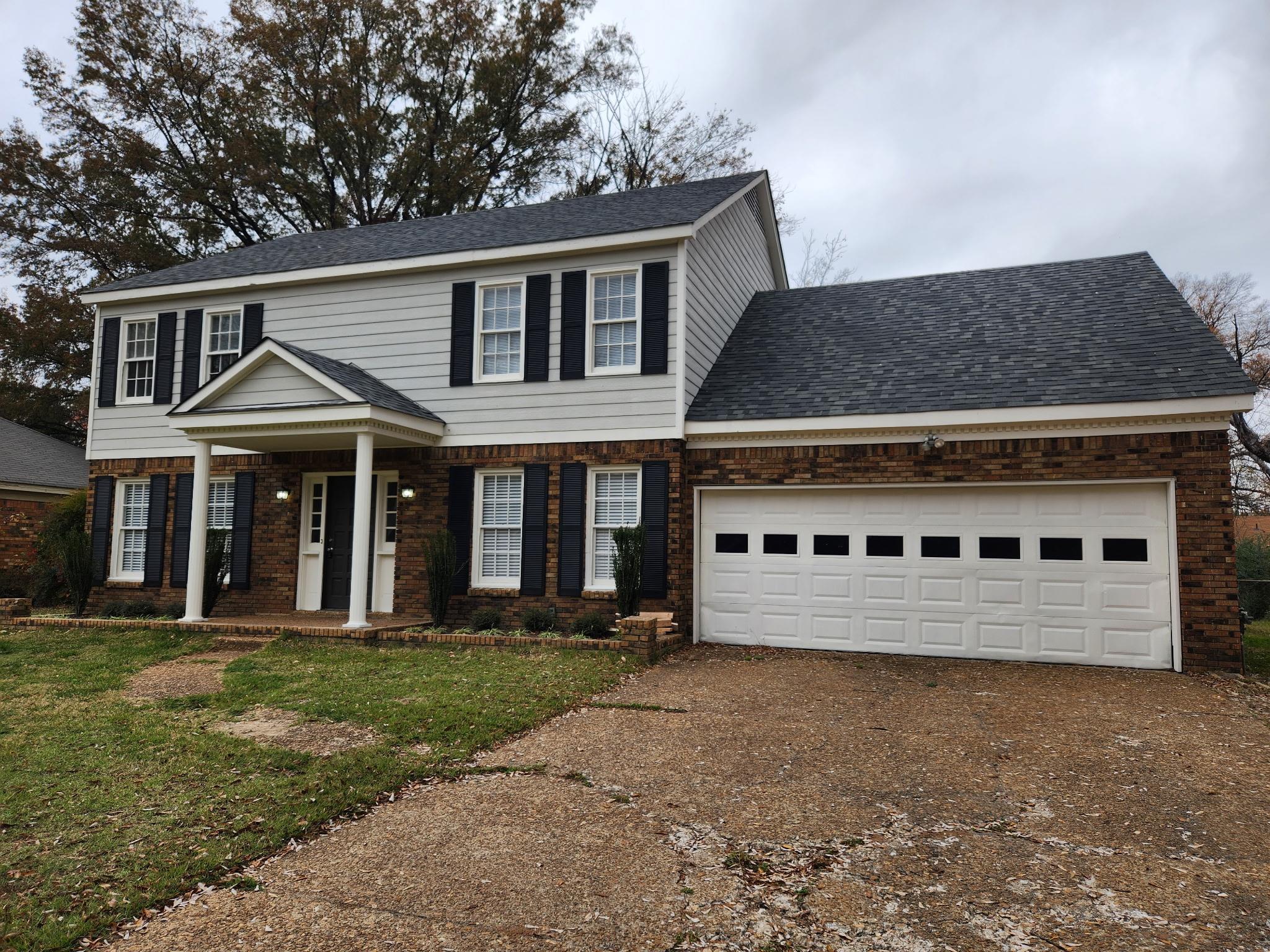 Traditional-style home with brick siding, a shingled roof, driveway, and a front yard