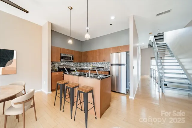 a kitchen with stainless steel appliances kitchen island granite countertop a dining table chairs and a refrigerator