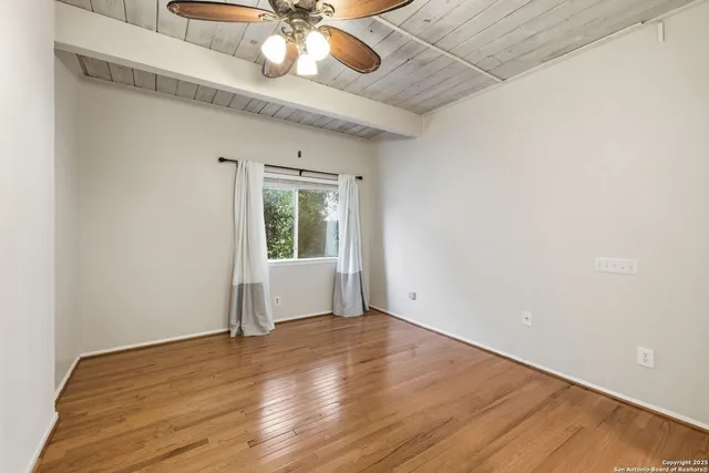an empty room with wooden floor fan and windows