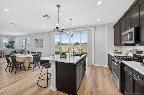 a kitchen with stainless steel appliances granite countertop a stove top oven a sink dishwasher a dining table and chairs with wooden floor