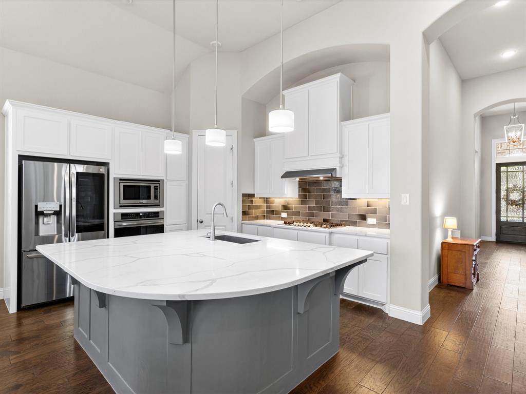 1630 Pebblebrook Lane Prosper, TX 75078 - Photo 15 of 40 a large kitchen with kitchen island a stove a sink a refrigerator and white cabinets with wooden floor