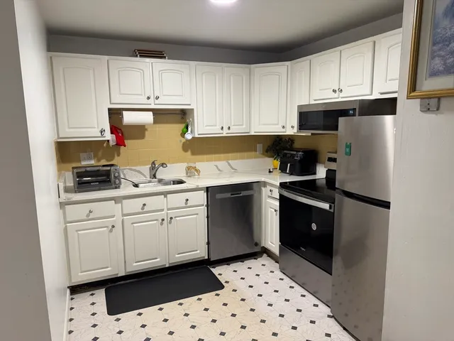 a kitchen with granite countertop a refrigerator sink and white cabinets