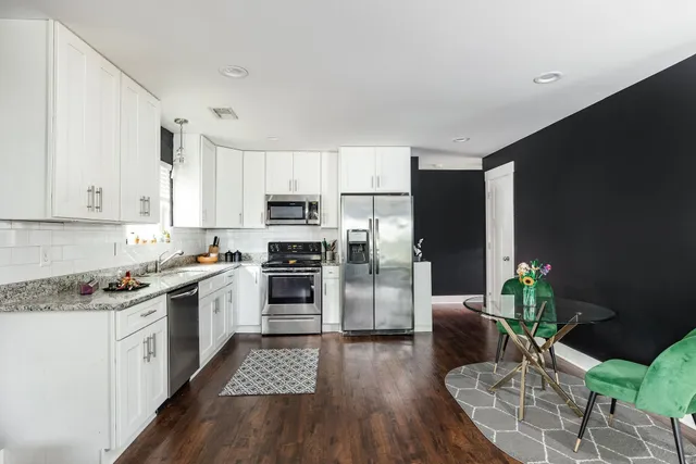 a kitchen with stainless steel appliances a microwave a stove a sink dishwasher a refrigerator white cabinets and wooden floor