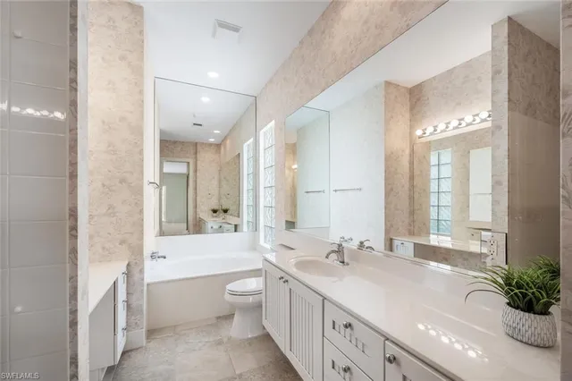 a spacious bathroom with a double vanity sink toilet mirror and bathtub