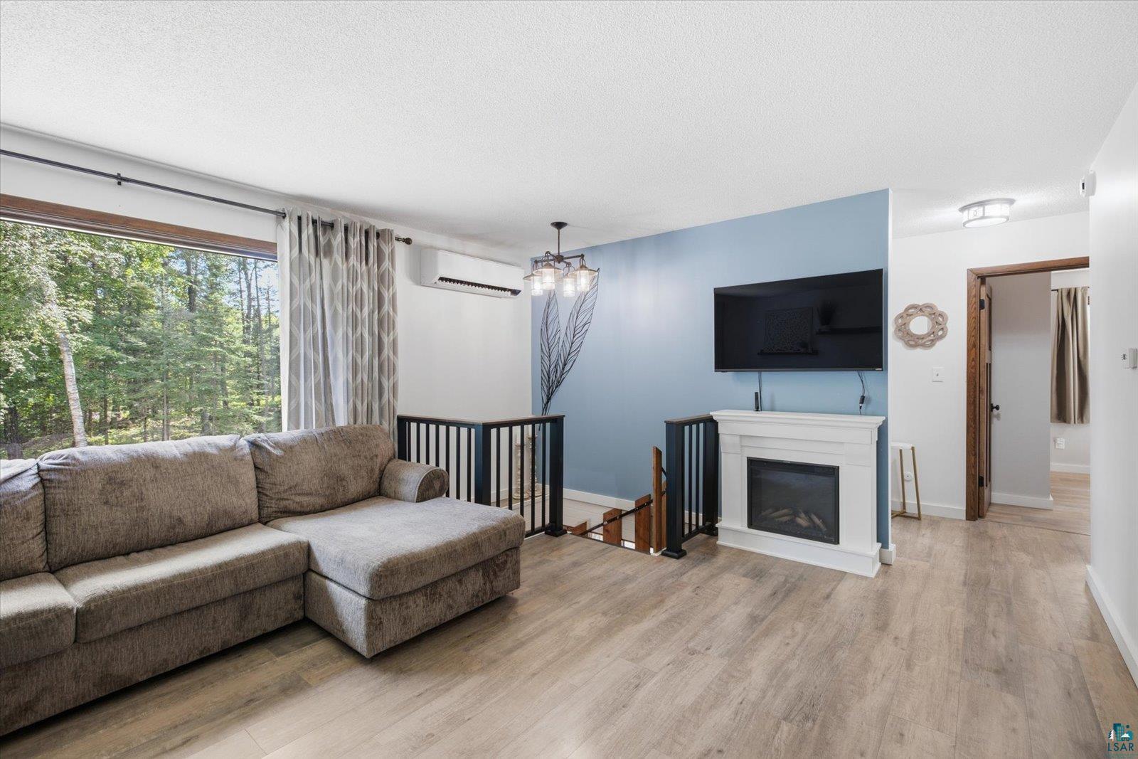 6377 Bergstrom Road Saginaw, MN 55779 - Photo 9 of 20 Living area featuring wood-finish flooring, a contemporary fireplace with white mantel, a mini-split system, and a black metal railing overlooking a lower level