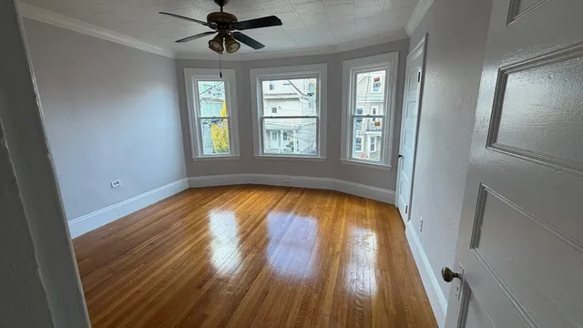a view of empty room with wooden floor and fan