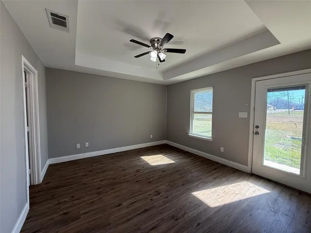 an empty room with wooden floor fan and windows