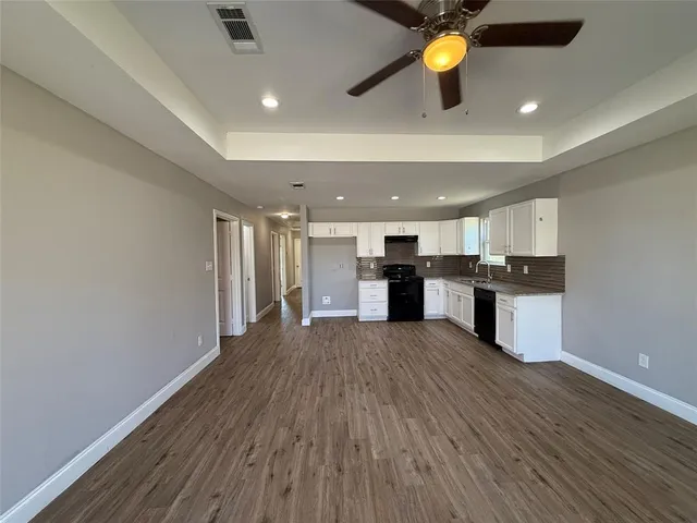 a view of an empty room and kitchen with wooden floor