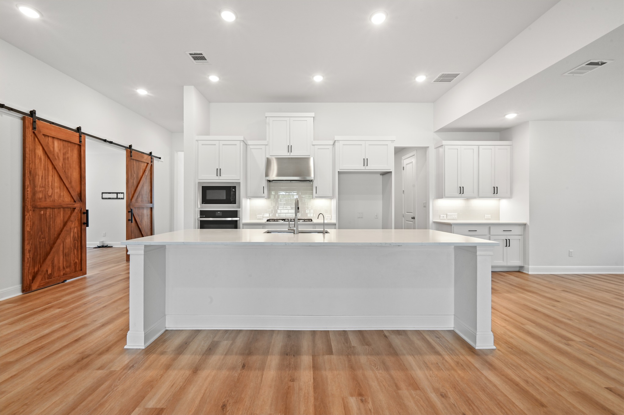433 Running Bird Road Austin, TX 78737 - Photo 10 of 40 A spacious, open-concept kitchen features bright white cabinetry, a large central island, and warm wood flooring.