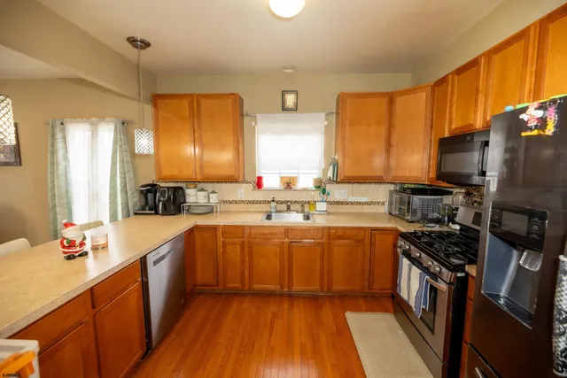 a kitchen with stainless steel appliances a sink dishwasher a stove top oven a refrigerator with wooden floor