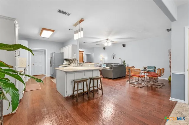 a open kitchen with stainless steel appliances a dining table chairs with wooden floor and chandelier