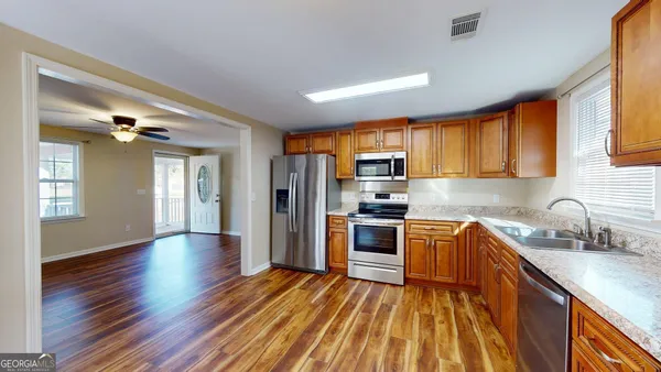 a kitchen with stainless steel appliances granite countertop a refrigerator a sink dishwasher a stove with wooden cabinets and floor