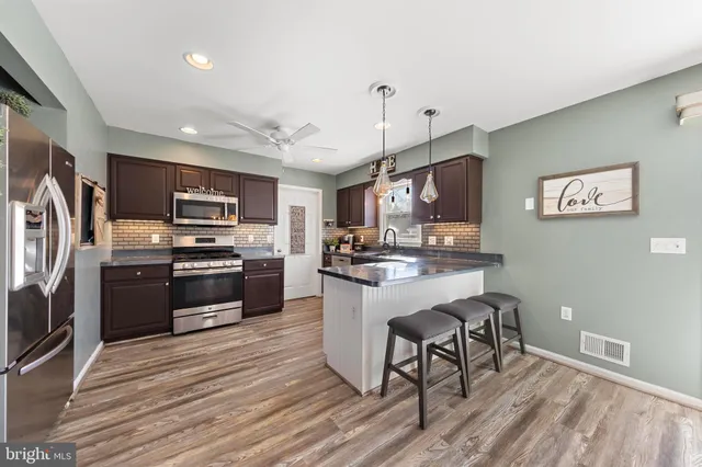 a kitchen with stainless steel appliances kitchen island granite countertop a refrigerator a stove top oven a sink dishwasher and white cabinets with wooden floor