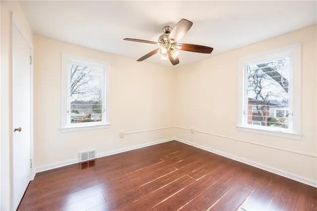 an empty room with wooden floor fan and windows