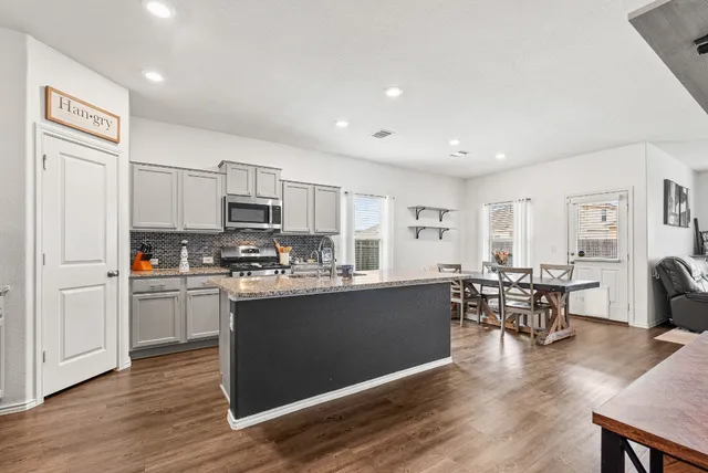 a kitchen with stainless steel appliances granite countertop a stove top oven a sink dishwasher a dining table and chairs with wooden floor