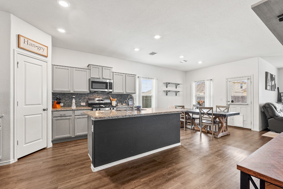 136 Copper Lane Kyle, TX 78640 - Photo 11 of 33 a kitchen with stainless steel appliances granite countertop a stove top oven a sink dishwasher a dining table and chairs with wooden floor