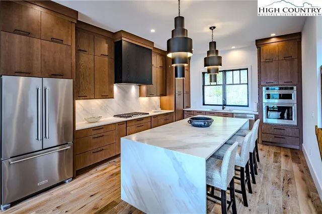 a kitchen with stainless steel appliances kitchen island granite countertop a refrigerator a stove and a wooden floors