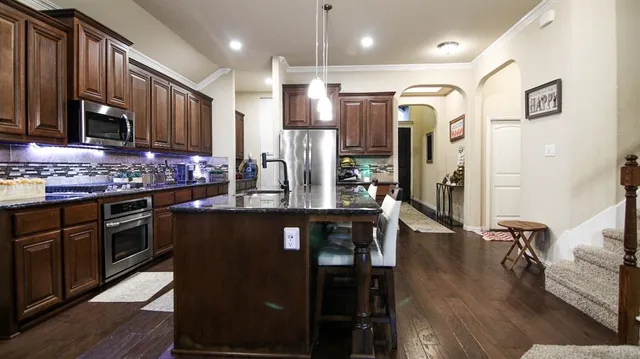 a kitchen with stainless steel appliances granite countertop a stove a refrigerator a sink a dining table and chairs with wooden floor