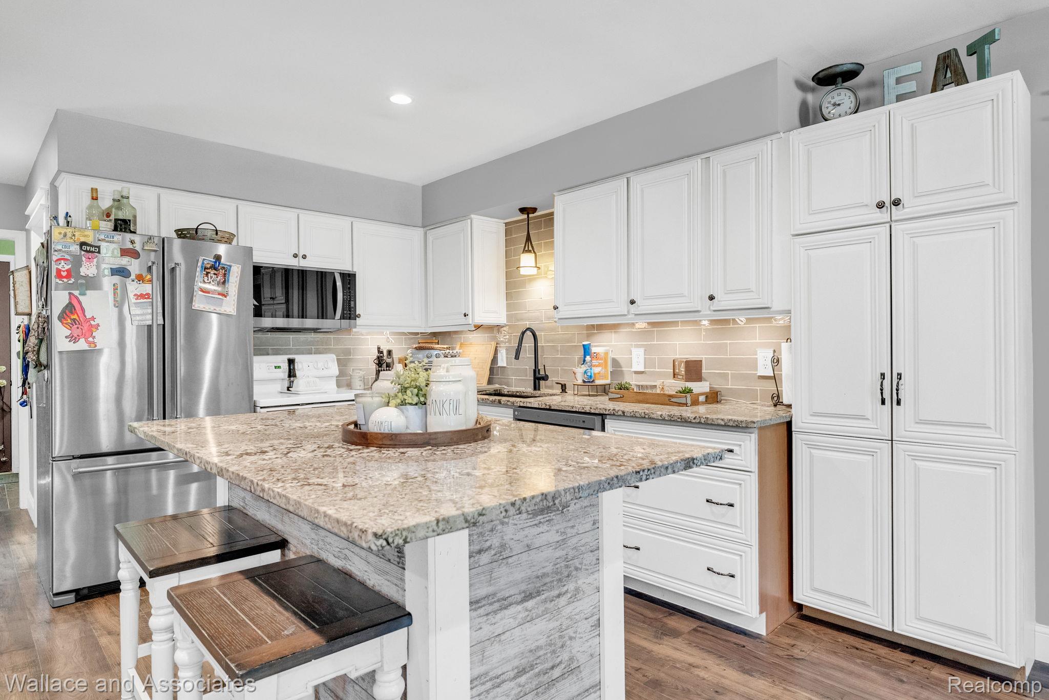 6616 Wellman Line Road Croswell, MI 48422 - Photo 21 of 47 Kitchen featuring stainless steel appliances, light stone countertops, white cabinets, a breakfast bar, and light wood-style flooring