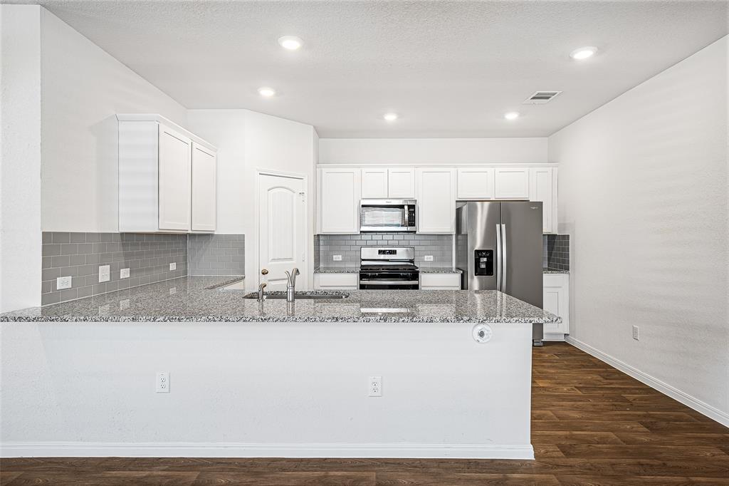 121 Mackinac Lane Georgetown, TX 78626 - Photo 3 of 16 a large kitchen with stainless steel appliances granite countertop a stove a sink a refrigerator and white cabinets with wooden floor