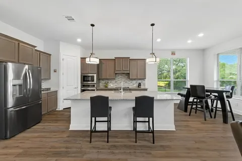 a kitchen with stainless steel appliances granite countertop a dining table chairs refrigerator and sink