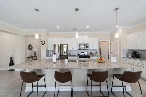 a kitchen with stainless steel appliances kitchen island granite countertop a dining table chairs sink and white cabinets