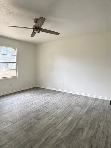 an empty room with wooden floor ceiling fan and windows