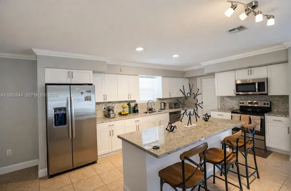 a kitchen with stainless steel appliances granite countertop a dining table chairs refrigerator and sink