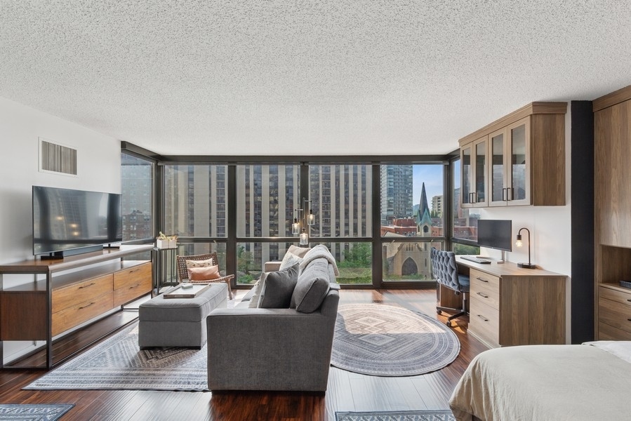 1122 North Clark Street, Unit 1002 Chicago, IL 60610 - Photo 3 of 14 a living room with furniture a flat screen tv and a floor to ceiling window