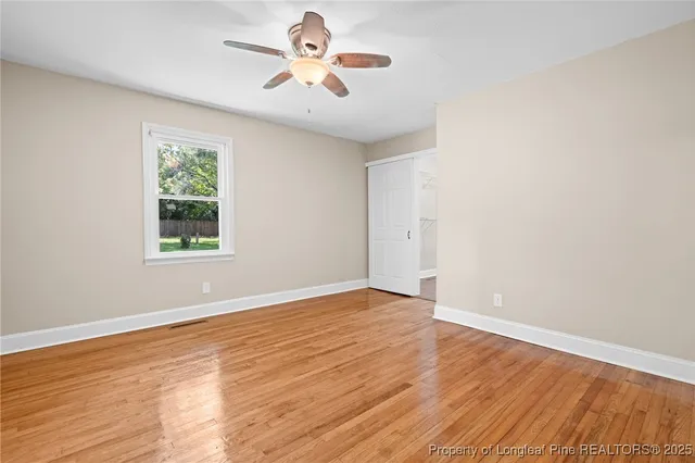 an empty room with wooden floor chandelier fan and windows