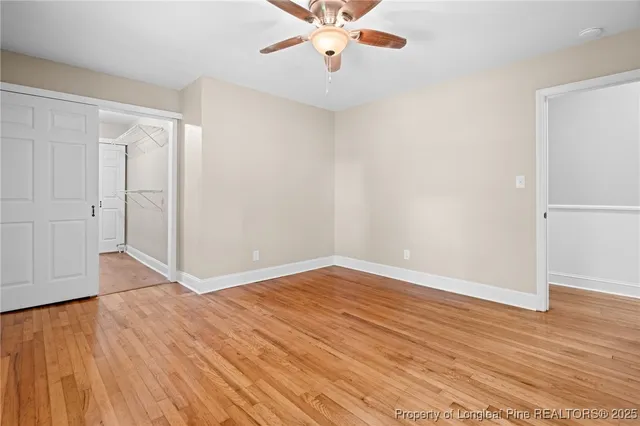 an empty room with wooden floor fan and windows