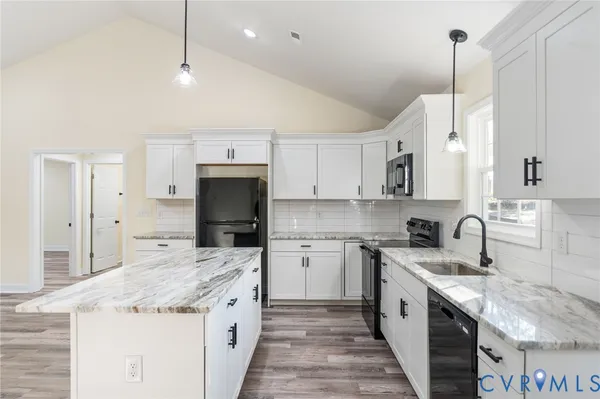 a kitchen with stainless steel appliances kitchen island granite countertop a refrigerator a sink dishwasher a stove and white cabinets with wooden floor