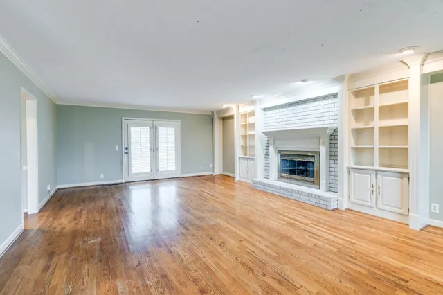 a view of an empty room with wooden floor fireplace and a window