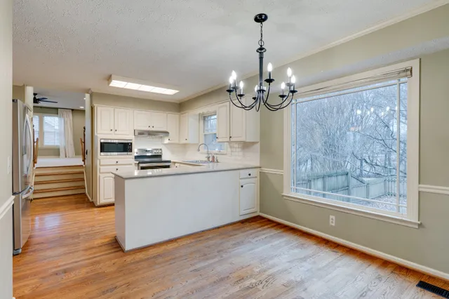 a kitchen with stainless steel appliances granite countertop a refrigerator a sink dishwasher a stove and white countertops with wooden floor