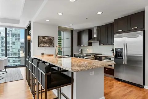 a kitchen with stainless steel appliances granite countertop a stove top oven a sink dishwasher a refrigerator and a dining table with wooden cabinet