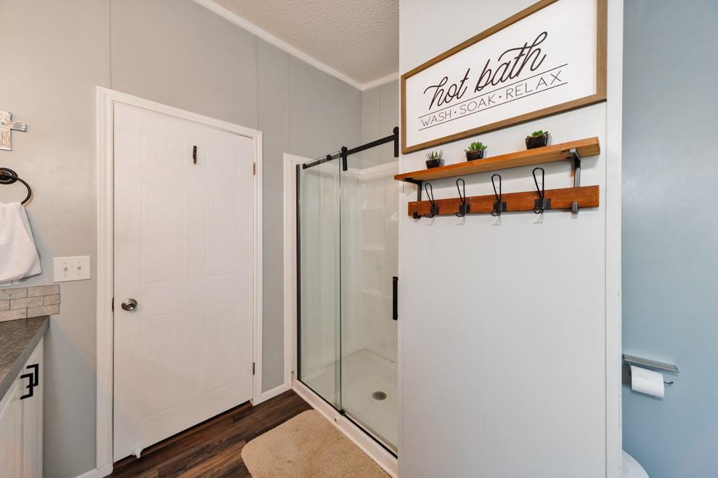 297 Lone Tree Lane Decatur, TX 76234 - Photo 12 of 20 Full bathroom with vanity, a shower stall, dark wood finished floors, a textured ceiling, and ornamental molding