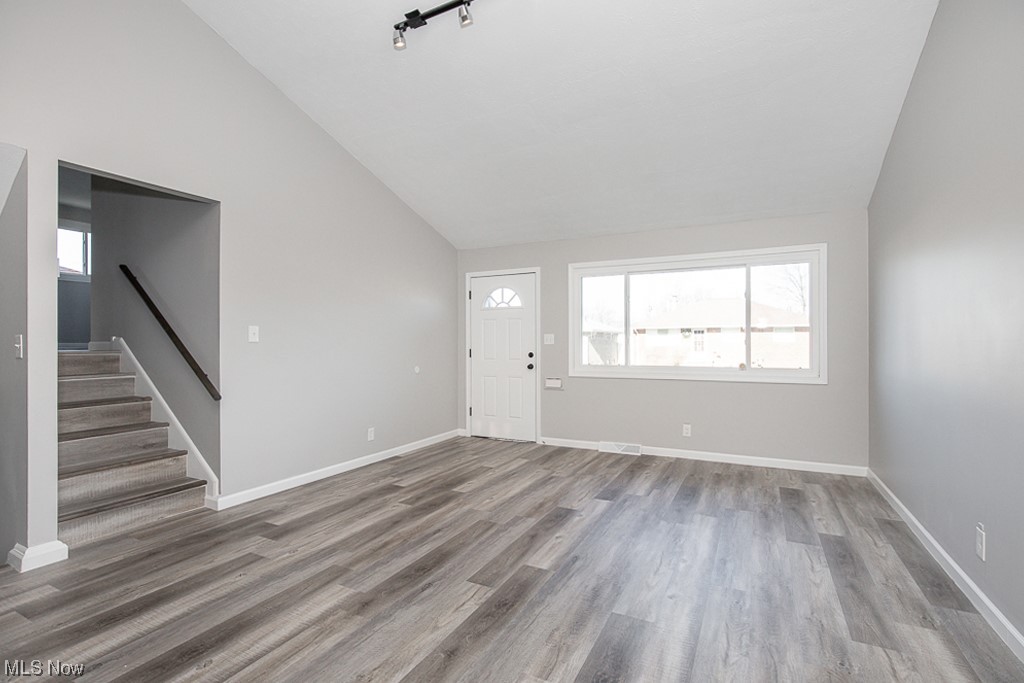 Living room featuring rail lighting, high vaulted ceiling, and light flooring