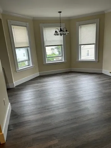 an empty room with wooden floor chandelier and windows