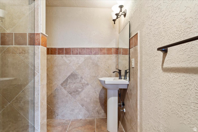246 Woods Creek Road Morgan, UT 84050 - Photo 69 of 69 Pedestal sink with dark bronze faucet, wall-mounted mirror, decorative wall sconce, full-height tile shower enclosure, and coordinating tiled walls