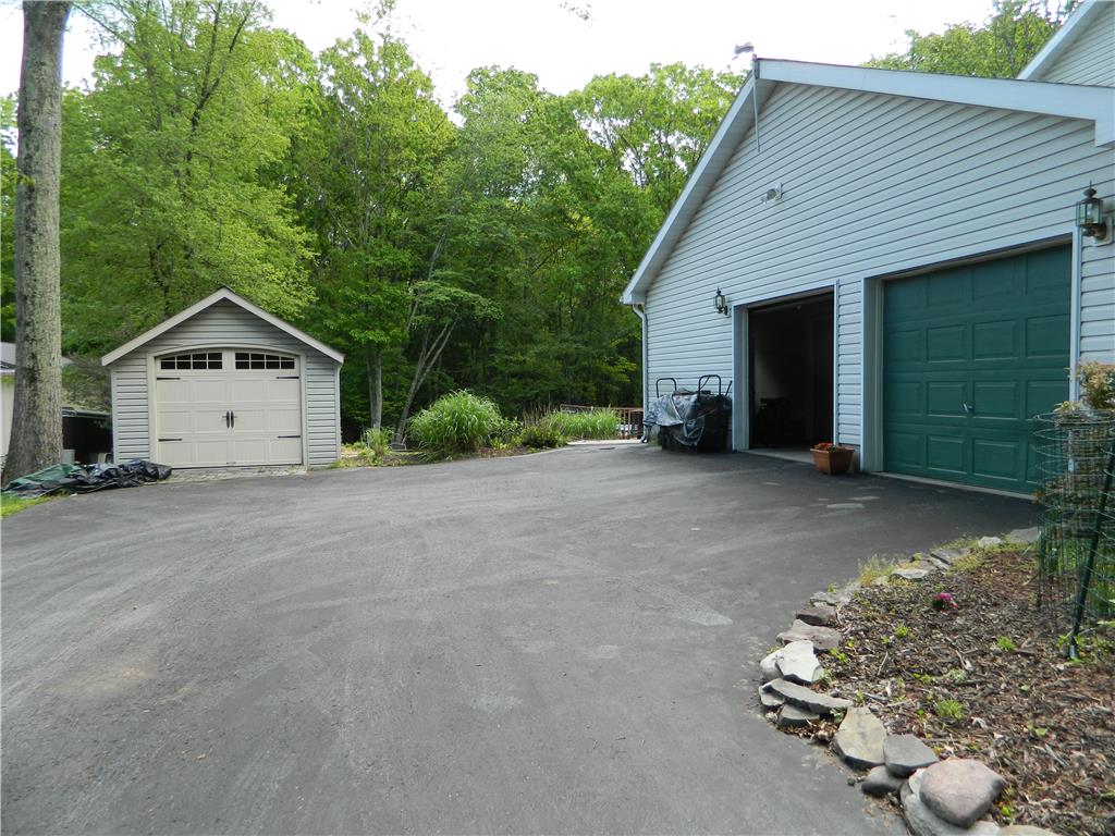 328 Pin Oak Road Stroudsburg, PA 18360 - Photo 2 of 37 A spacious asphalt driveway leads to a garage and a detached shed, set against a backdrop of mature trees.
