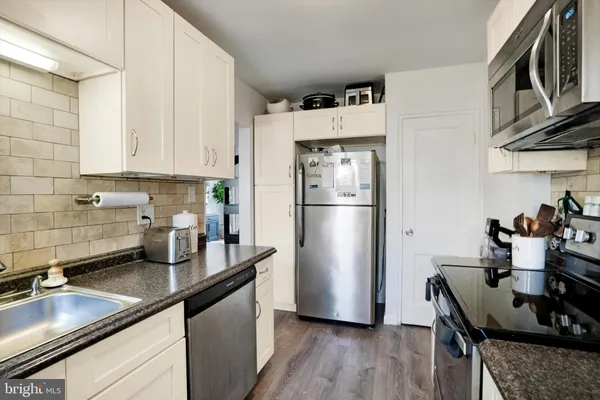 a kitchen with stainless steel appliances granite countertop a refrigerator a sink a stove and white cabinets