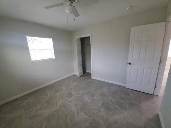 an empty room with a window and chandelier fan