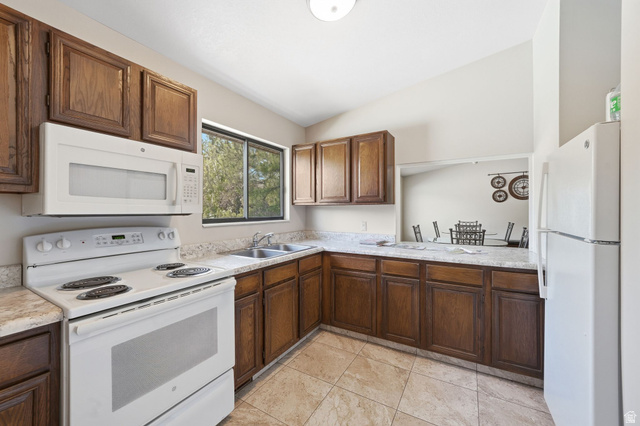 6969 South 855 East Midvale, UT 84047 - Photo 44 of 55 Kitchen featuring wood cabinetry, solid surface countertops, white appliances, a double basin sink, and tile flooring