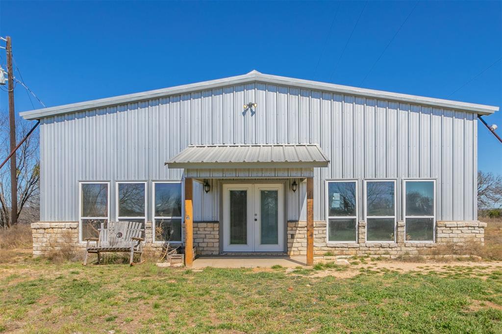 View of front of home featuring board and batten siding, stone siding, a front lawn, and french doors