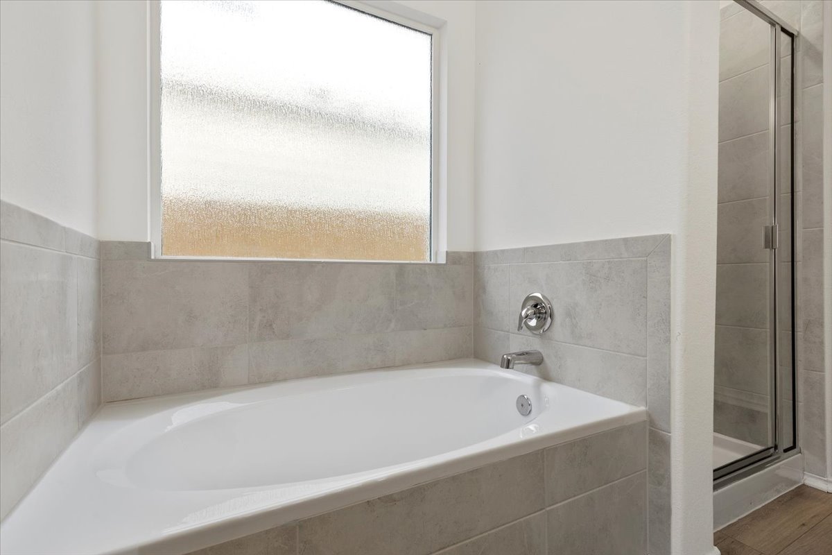 101 Rowdy Yates Way Jarrell, TX 76537 - Photo 19 of 32 Soaking tub with chrome fixtures, surrounded by light-toned tile, with a frosted window and glass-enclosed shower