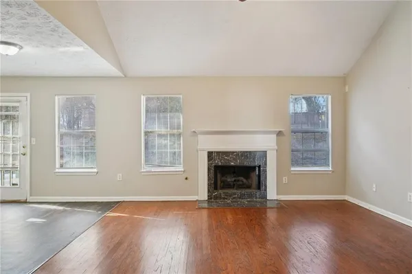 an empty room with wooden floor fireplace and windows