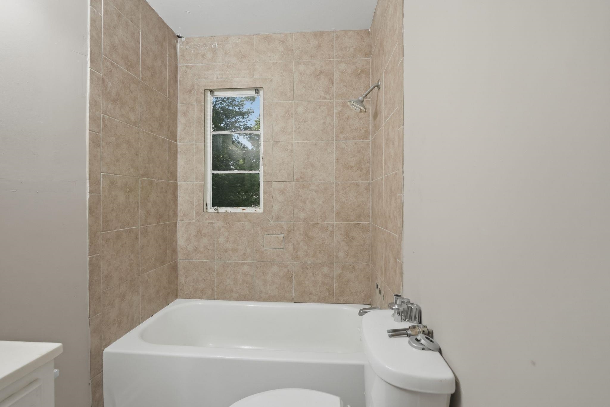 4955 Stacey Road Memphis, TN 38109 - Photo 31 of 35 Bathroom featuring a white bathtub, ceramic tile surround, and a window for natural light