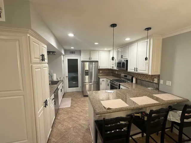 a kitchen with stainless steel appliances kitchen island granite countertop a refrigerator a stove a sink a dining table and chairs