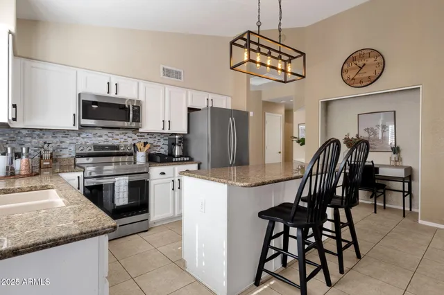 a kitchen with stainless steel appliances granite countertop a refrigerator a sink a stove a dining table and chairs