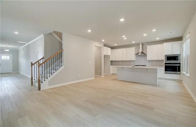 a view of an empty room and kitchen with wooden floor
